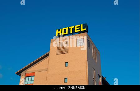 Insegna dell'hotel con la parola HOTEL illuminata di giallo sullo sfondo di un cielo azzurro. Il cartello si trova sulla sommità di un edificio color marrone Foto Stock