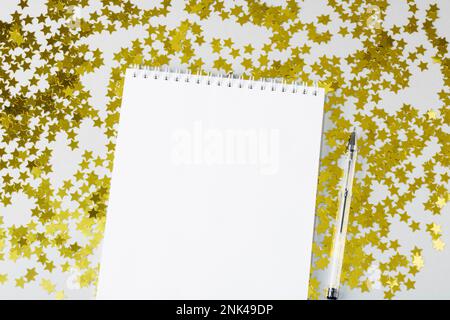 Composizione di Natale. Natale, concetto di Capodanno. Un taccuino bianco aperto su uno sfondo di coriandoli di stelle accanto ad una penna. Natale e. Foto Stock