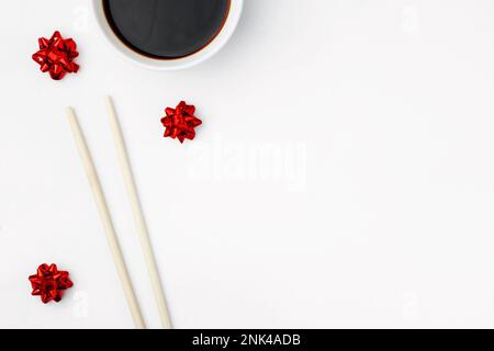 I bastoncini di sushi di bambù sono isolati su uno sfondo bianco, accanto alla salsa di soia e alle archi rossi. Concetto sfondo festivo, biglietto d'auguri, menu per orientale r Foto Stock