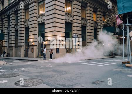 New York, USA - 25 novembre 2022: Vapore che sale da una bocca in una strada nel Financial District, il cuore finanziario di New York e una casa di Wall Street. Foto Stock