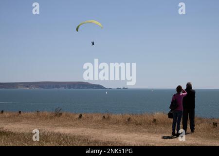 Una coppia guarda un parapendio in aria a Barton-on-Sea, South Coast of England con l'Isola di Wight in lontananza, Regno Unito Foto Stock