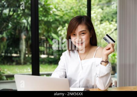 Sorridente bella donna asiatica presentando carta di credito in mano mostrando fiducia e fiducia per effettuare il pagamento. Concetto di shopping online. Foto Stock