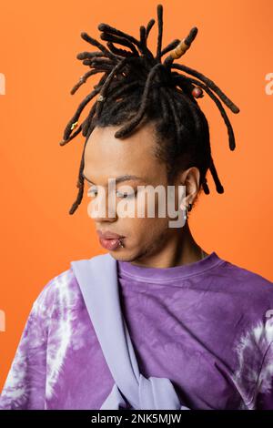 ritratto di uomo multirazziale con greggi e piercing isolato su arancione, immagine stock Foto Stock
