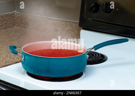 Shot orizzontale di una pentola blu su un piano cottura che contiene zuppa di pomodoro fumante. Foto Stock