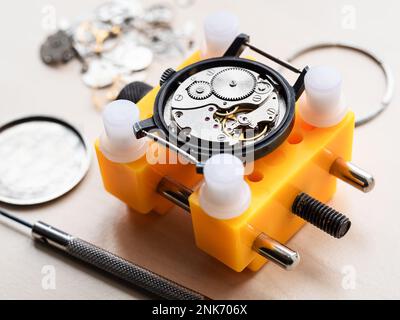 vecchio orologio meccanico in supporto giallo primo piano su tavolo in legno in officina orologiaio Foto Stock
