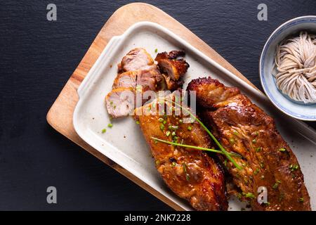 Concetto di cucina casalinga Char siu stile cantonese di maiale alla griglia su sfondo di pietra ardesia nera con spazio copia Foto Stock