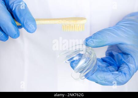 Foto ravvicinata dei medici mani in guanti con protezione bocca in silicone e spazzolino in legno. Cura dei denti. Foto Stock