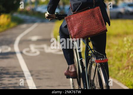 Vista rifilata del manager maschile anonimo in tuta alla moda che corre sulla pista ciclabile dopo il lavoro. Elegante executive con una costosa valigetta in pelle che si presenta a WO Foto Stock