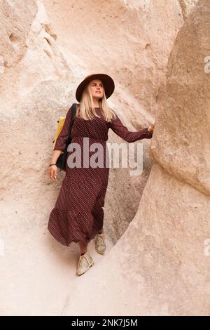 Donna in viaggio che indossa un cappello marrone e un abito lungo camminando nelle rocce di sabbia della valle. Concetto di viaggio e di vagabondo. Foto Stock