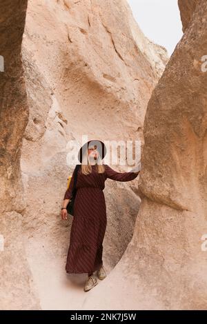 Donna in viaggio che indossa un cappello marrone e un abito lungo camminando nelle rocce di sabbia della valle. Concetto di viaggio e di vagabondo. Foto Stock