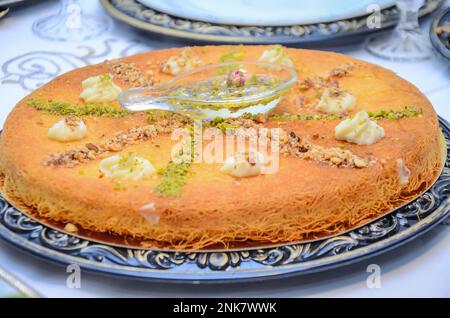 Kunafa dessert orientale in un grande piatto Vista dall'alto. Kunafa al formaggio arabo al buio. Konafa. Foto Stock