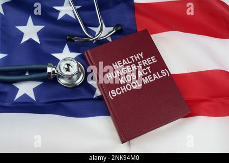 Concetto di legge. Sulla bandiera degli Stati Uniti si trova uno stetoscopio e un libro con l'iscrizione - ATTO SANO BAMBINI SENZA FAME - PASTI SCOLASTICI Foto Stock