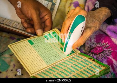 Yazd, Iran - 22nd giugno, 2022: Donna anziana a casa uso corano elettrico leggere penna per leggere in arabo Foto Stock