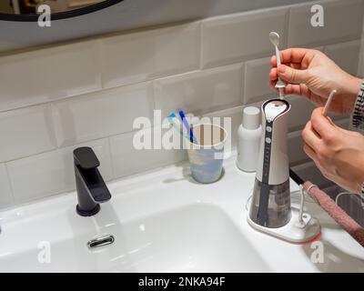 Le mani del giovane uomo che cambiano la sua punta domestica del flosser dell'acqua dentale Foto Stock