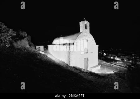 Vista di una piccola chiesa illuminata imbiancata a iOS Greece in cima alla collina Foto Stock