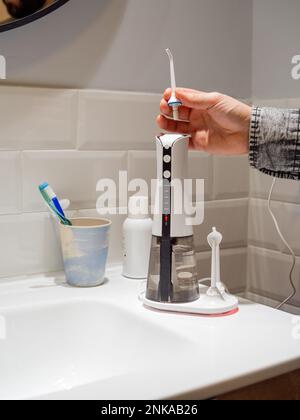 Le mani del giovane uomo che cambiano la sua punta domestica del flosser dell'acqua dentale Foto Stock