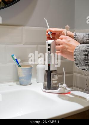 Le mani del giovane uomo che cambiano la sua punta domestica del flosser dell'acqua dentale Foto Stock