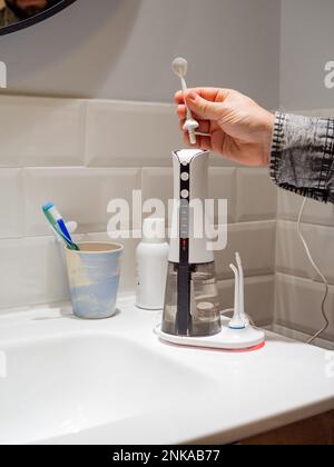 Le mani del giovane uomo che cambiano la sua punta domestica del flosser dell'acqua dentale Foto Stock