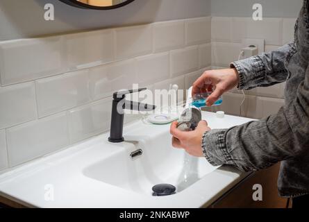 Senza sforzo Salute orale: Uomo riempimento acqua serbatoio flosser con collutorio al bagno bacino Foto Stock