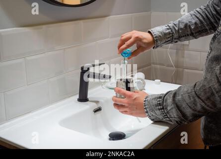 Senza sforzo Salute orale: Uomo riempimento acqua serbatoio flosser con collutorio al bagno bacino Foto Stock