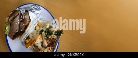 Un giroscopio greco mediterraneo avvolto in un foglio su un piatto con un lato di patatine fritte greche ricoperte di mozzarella e formaggio feta fuso, erbe aromatiche e spezie Foto Stock