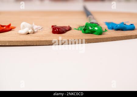 Tavolozza di legno con pitture ad olio colorato e pennelli isolati su sfondo bianco Foto Stock