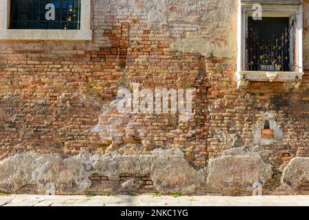 La finestra bianca sul muro della vecchia casa si rompe in mattoni rossi visibili in cemento a Venezia. Foto Stock