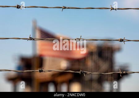 Detroit, Michigan, una bandiera americana vola dietro una recinzione di filo spinato in un cantiere edile Foto Stock