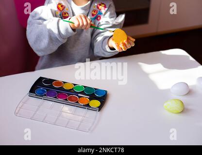 Primo piano delle mani dei bambini che tengono l'uovo di pasqua e dipingono con un pennello a casa. Preparandosi per pasqua. Buona Pasqua. Foto Stock