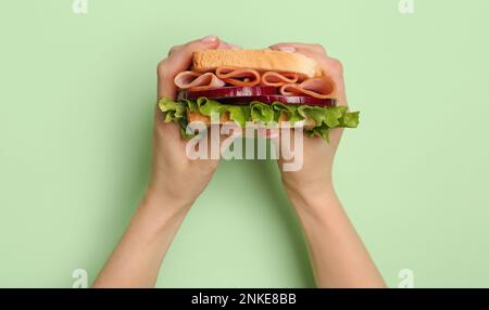 Le mani femminili tengono un delizioso sandwich al prosciutto su sfondo verde Foto Stock