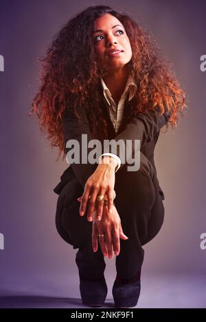 Ritratto integrale di bella Donna con pelle nera e lunghi capelli ondulati, elegantemente vestita, squatting come lei guarda divertito e premuroso. 1980s Foto Stock