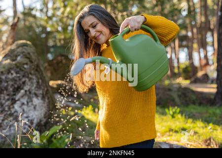 Donna matura impianto di irrigazione in giardino Foto Stock