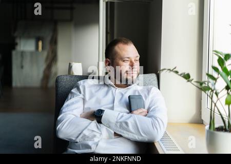 Uomo d'affari che prende una pausa in ufficio guardando fuori dalla finestra Foto Stock