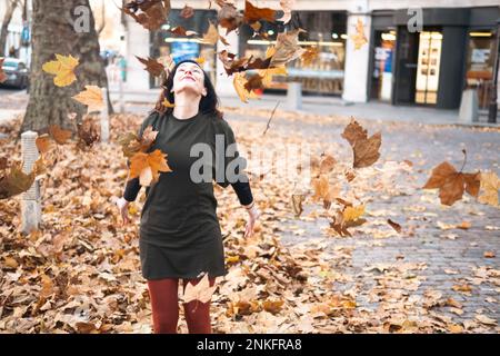 Donna che gioca con foglie autunnali sul sentiero Foto Stock