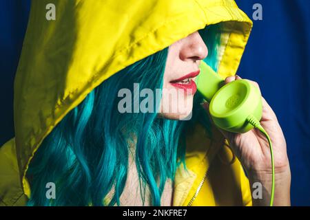 Donna che indossa una camicia gialla con cappuccio che parla sul telefono verde Foto Stock