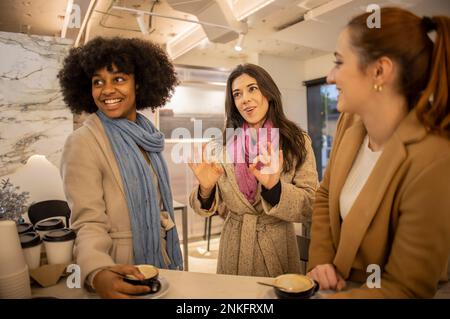 Donna felice che mostra un gesto OK con gli amici in piedi al tavolo Foto Stock
