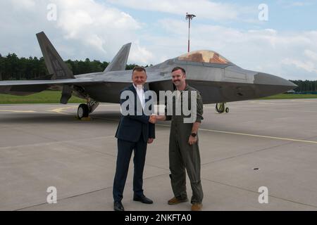 Il vice primo ministro polacco, il ministro della Difesa nazionale Mariusz Błaszczak e il sig. Michael Kendall, comandante del combattente espeditionale Squadron del 90th, stringono le mani davanti agli Stati Uniti Air Force F-22 e Polish Air Force F-16 presso la base aerea di Łask, Polonia, 14 agosto 2022. Gli Stati Uniti e la Polonia condividono un impegno costante a garantire la sicurezza e la stabilità del fianco orientale della NATO. Foto Stock