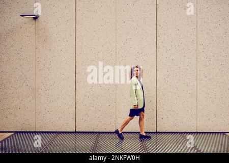 Donna d'affari che cammina di fronte al muro Foto Stock