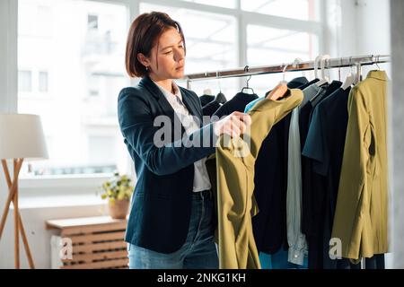 Giovane donna d'affari che sceglie dalla cremagliera dell'abbigliamento in ufficio Foto Stock