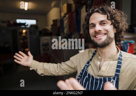 Felice giovane uomo d'affari che indossa grembiule invitante in deposito Foto Stock
