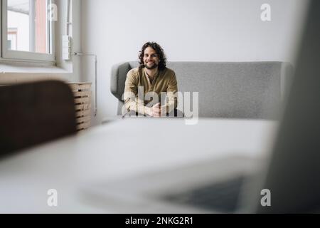 Buon giovane uomo d'affari seduto sul divano sul posto di lavoro Foto Stock