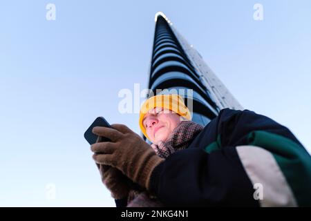 Persona non binaria che utilizza lo smartphone di fronte all'edificio Foto Stock