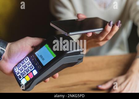 Mano di donna che effettua il pagamento tramite smartphone al caffè Foto Stock