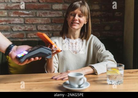 Donna sorridente che effettua il pagamento tramite smartphone al bar Foto Stock