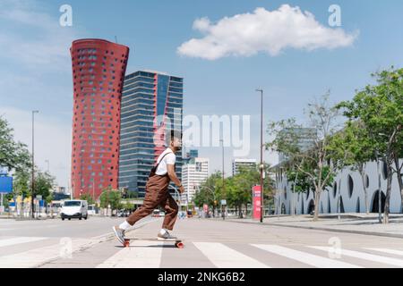 Giovane uomo skateboard sulla zebra traversata in città Foto Stock