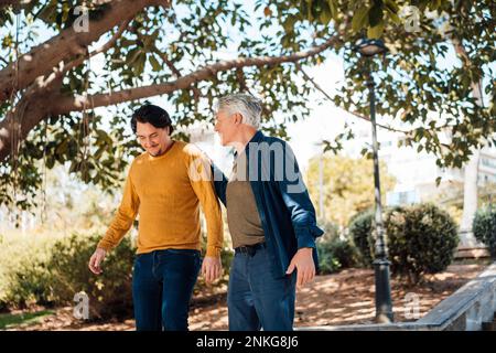 Felice padre e figlio che camminano insieme davanti all'albero Foto Stock