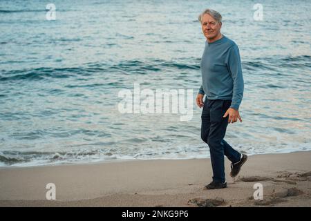 Un uomo anziano sorridente che cammina sulla spiaggia Foto Stock