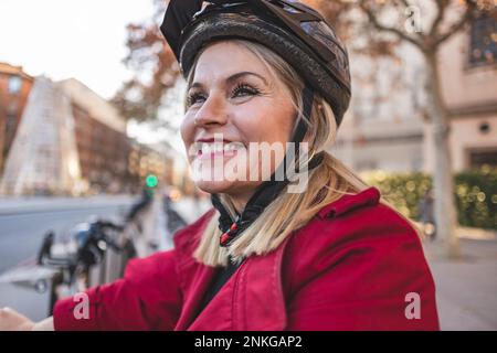 Donna matura allegra cavalcando il casco da bicicletta Foto Stock