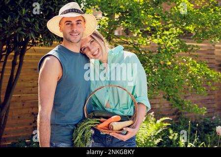 Felice giovane coppia in piedi con cestino di verdure in giardino Foto Stock