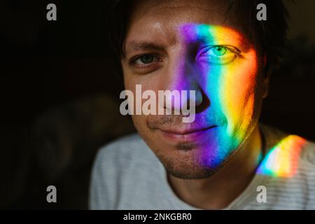 Uomo sorridente con luce arcobaleno sul viso Foto Stock